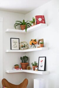 Planters, books and wall art on living room corner floating shelves
