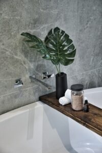 A fake plant placed on a wooden bar that’s placed on what looks like a bathtub