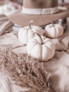 Three white pumpkins beside a hat, sweaters, and dried leaves