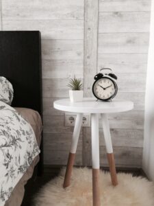 A plant and a clock on a three-legged bedside table